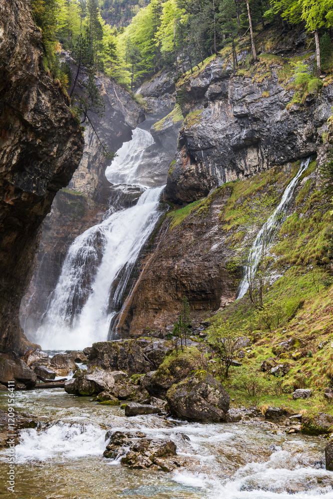 Cascada del estrecho, waterfall flowing through rocky cliffs surrounded by lush greenery in Ordesa y Monte Perdido National Park, Spanish Pyrenees Cascada del estrecho, waterfall flowing through rocky cliffs surrounded by lush greenery in Ordesa y Monte Perdido National Park, Spanish Pyrenees