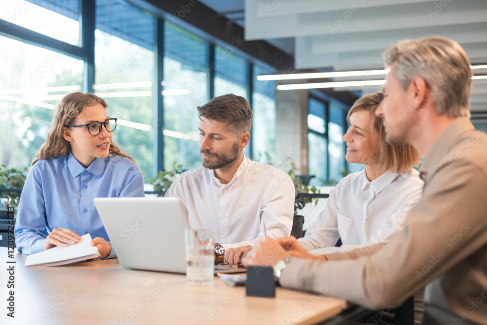 Four business people discussing work together using a tablet and laptop taking notes in a modern office Four business people discussing work together using a tablet and laptop taking notes in a modern office
