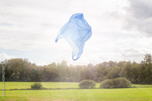environmental plastic waste pollution in nature: disposable plastic bag flies over idyllic countryside