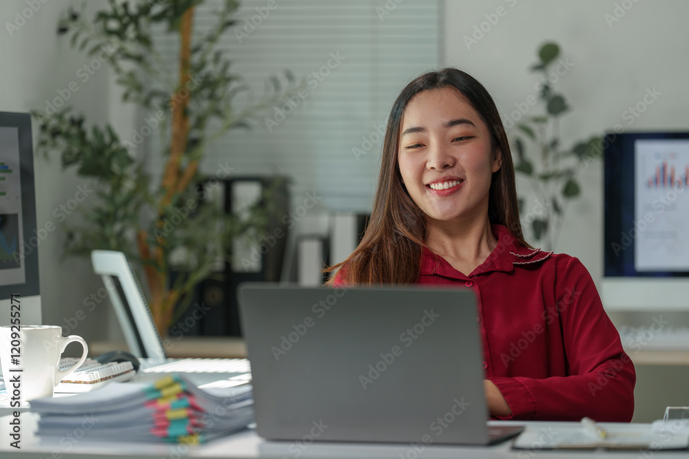 Young asian businesswoman smiling and working on a laptop in a modern office, benefiting from natural light and a productive environment, surrounded by technology and documents Young asian businesswoman smiling and working on a laptop in a modern office, benefiting from natural light and a productive environment, surrounded by technology and documents