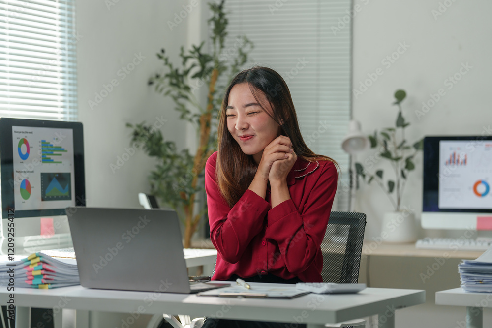 Young asian businesswoman with a happy expression is sitting at her desk in a modern office, using a laptop and enjoying her work, surrounded by computer screens displaying charts and graphs Young asian businesswoman with a happy expression is sitting at her desk in a modern office, using a laptop and enjoying her work, surrounded by computer screens displaying charts and graphs