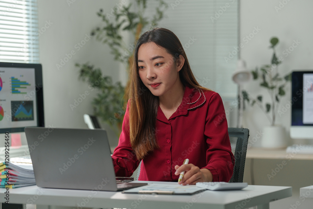 Young professional woman working on a laptop, analyzing financial statistics on the screen while preparing a report with business documents and diagrams Young professional woman working on a laptop, analyzing financial statistics on the screen while preparing a report with business documents and diagrams