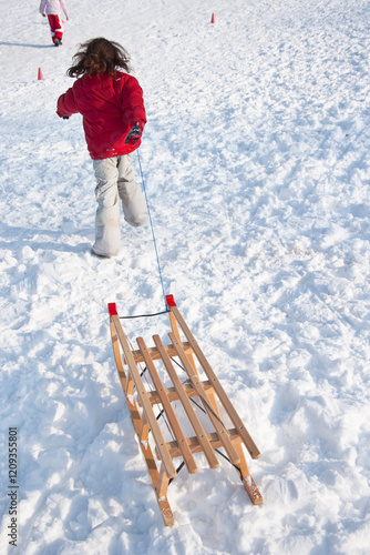 A joyful scene of a child pulling a wooden sled through the soft, powdery snow creates a captivating winter moment, evoking feelings of childhood joy and adventure. photo