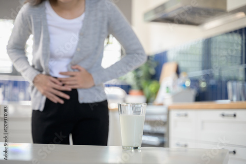 Allergy dairy food lactose intolerance allergen health care illness concept. Close up a glass of milk with blurred Asian woman holding stomach belly feel pain digestive unhappy after drink a cow milk. photo