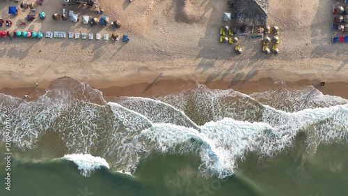 A drone shot captures Goa's stunning beachside, with golden sands stretching along the coastline, waves crashing gently, and lush greenery bordering the shore.