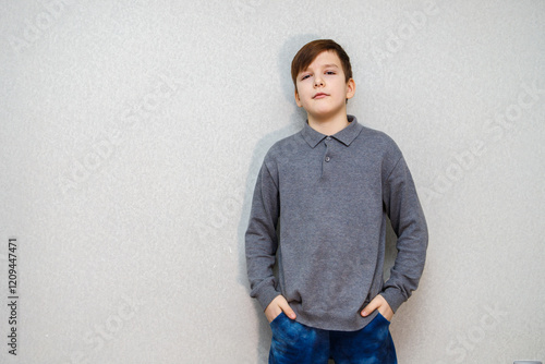 A ten year old boy in a gray sweater stands against the wall. Hands in pockets photo