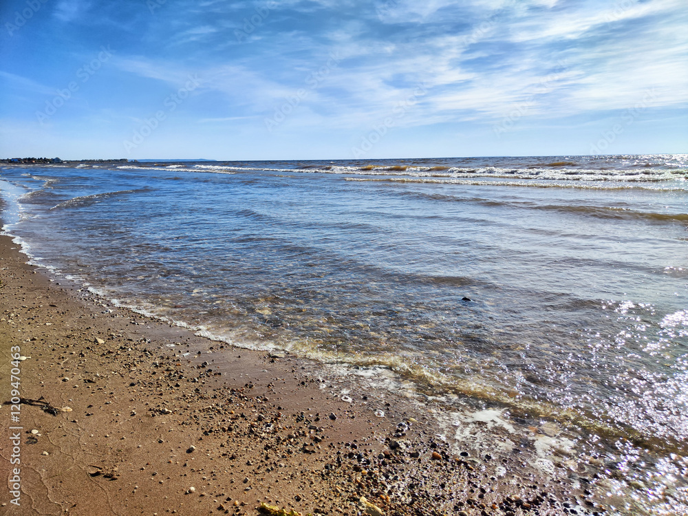 Waves gently lap the sandy shore on a sunny day by the tranquil coastline Waves gently lap the sandy shore on a sunny day by the tranquil coastline