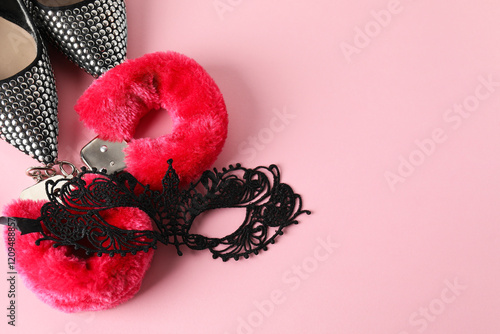 Fluffy handcuffs, lace mask and high-heeled shoes on pink background, flat lay. Space for text photo