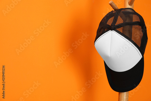 Fotografía Stylish baseball cap on coat rack against orange wall