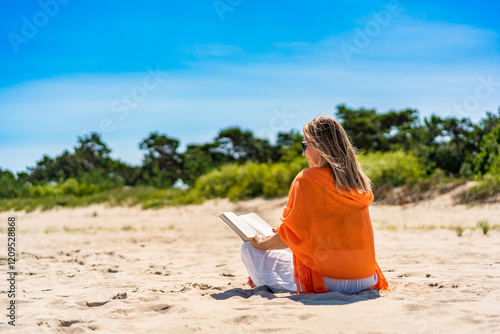 Beautiful mature woman sitting on white sandy beach reading book in summer. Back view #1209528868