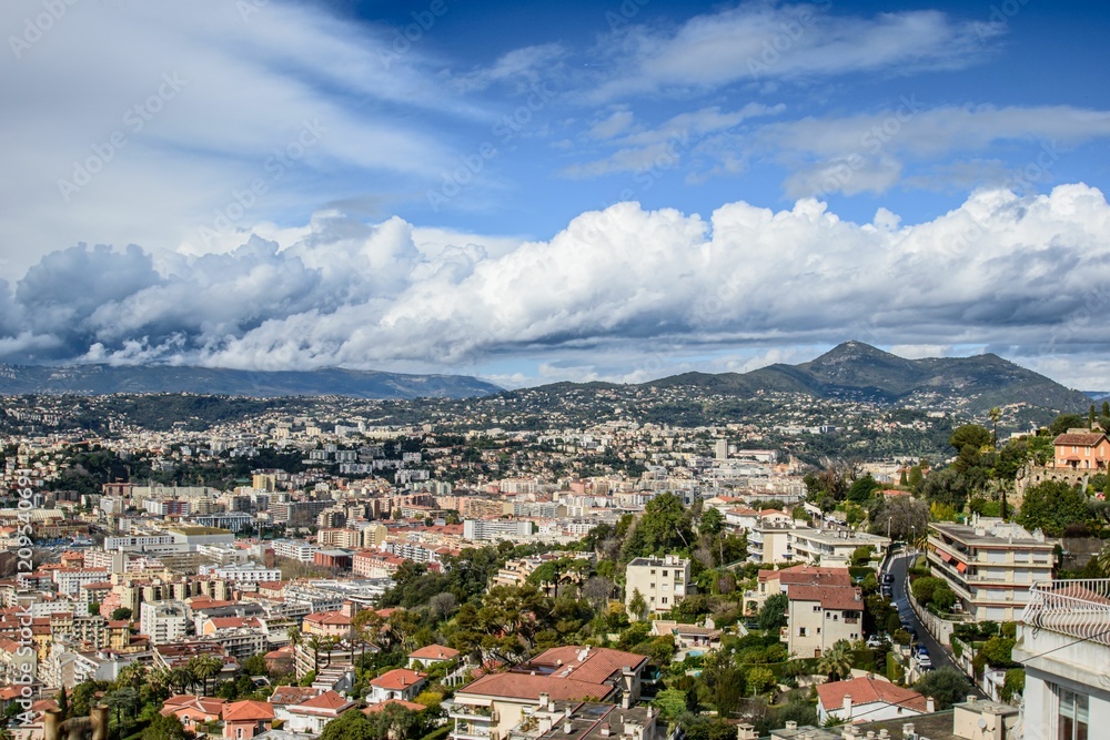 Fototapeta premium Scenic view of Nice, France with a backdrop of mountains and a partly cloudy sky.
