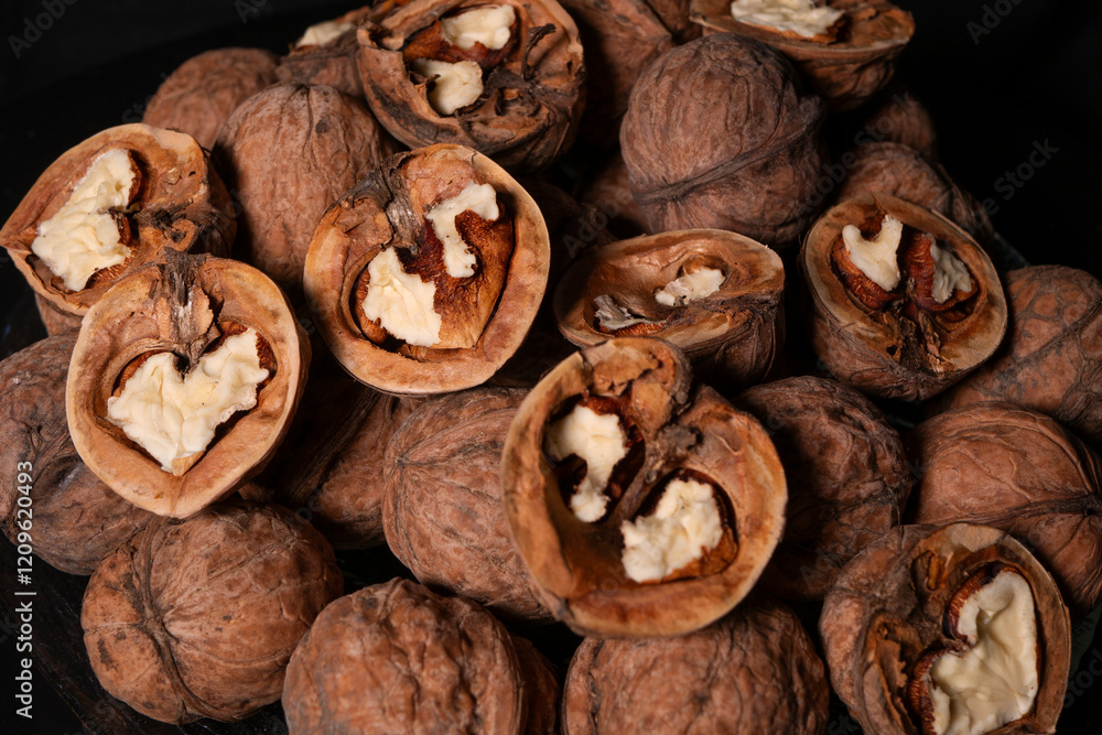 Peeled and whole walnuts lie on a glass plate. Black background. Peeled and whole walnuts lie on a glass plate. Black background.