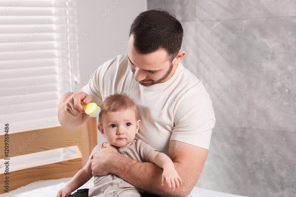 Man brushing hair of his little baby on bed indoors Man brushing hair of his little baby on bed indoors