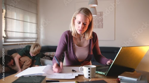 A mother works from home on her laptop in the living room, trying to focus on her tasks, while yelling at her children to calm down as they play energetically in the background.