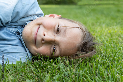 close-up of the cute face of an 8 year old boy lying on the grass. joy of childhood, positive. Hello summer, energy of nature. Earth Day photo