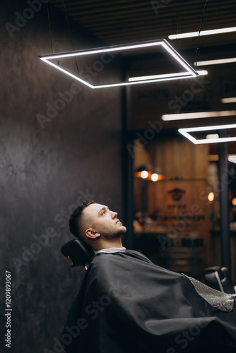 a photo of a professional barber focusing on the work of a client in a barber chair in front of a mirror in a modern barbershop
