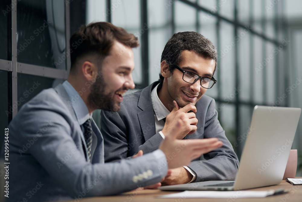 Fototapeta premium Two young businessmen sitting at workplace and working together in office