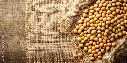 Top view of yellow soybeans scattered on a textured burlap cloth with a rustic wooden background offering ample space for design elements.