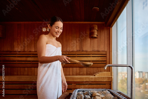 Happy woman pouring water over hot stones in sauna. photo