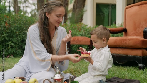In Moroccan garden, mother and son enjoy raspberry-topped pastry together during picnic near their home. They share dessert in warm and relaxed outdoor setting. Concept of family bonding, sweet moment