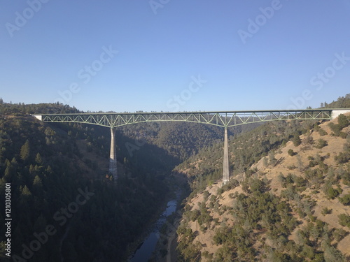 Majestic drone shot of Foresthill Bridge, California's iconic landmark, spanning the American River, capturing the beauty of its engineering marvel amidst the serene backdrop of rolling hills and tree