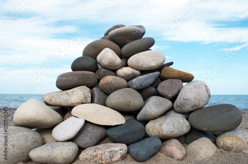 Triangular pile of stones stacked in foreground with blue sky white cloud background on beach