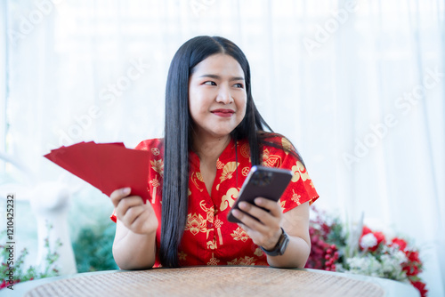 Obraz na płótnie Portrait of asian woman wearing red cheongsam dress holding red envelopes and smartphone at home in the living room indoor decoration for Chinese new year festival celebrate culture of china holiday w salonie