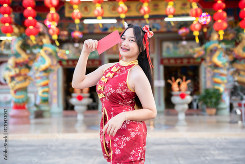 Portrait smiles Asian young woman wearing red cheongsam dress holding red envelopes decoration for Chinese new year festival celebrate culture of china at Chinese shrine Public places in Thailand