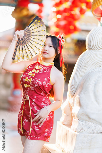 Obraz na płótnie Portrait beautiful cute smiles Asian young woman wearing red traditional Chinese cheongsam decoration and holding a Chinese Fanning for Chinese New Year Festival at Chinese shrine in Thailand w salonie