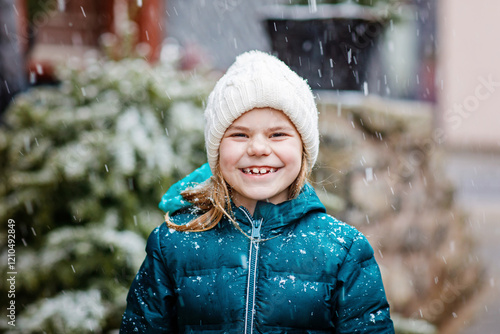 Funny portrait of little school girl in winter clothes. Happy positive child outdoors. Winter day, snow falling. Cold weather and snowing. photo