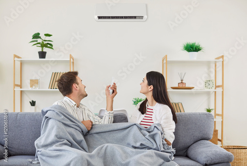 Obraz na płótnie Family couple resting on sofa operates and turn on a wall-mounted air conditioner at home, focusing on climate control, comfort, and managing air conditions for a pleasant indoor environment
