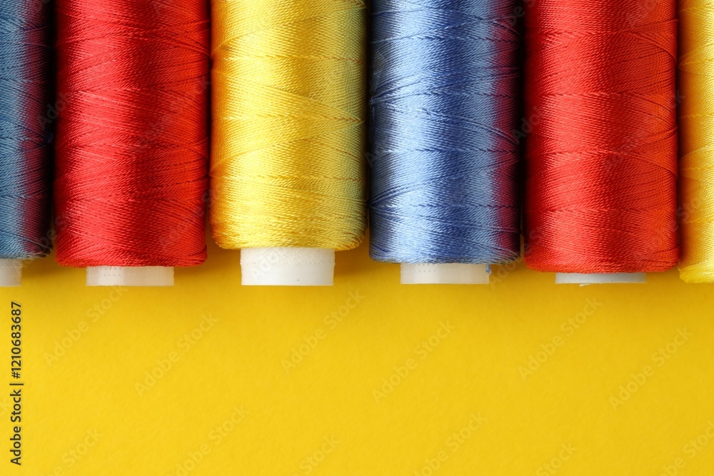Different spools of sewing threads on yellow background, flat lay. Space for text Different spools of sewing threads on yellow background, flat lay. Space for text