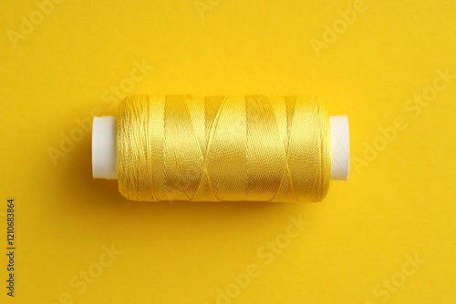 Spool of sewing thread on yellow background, top view