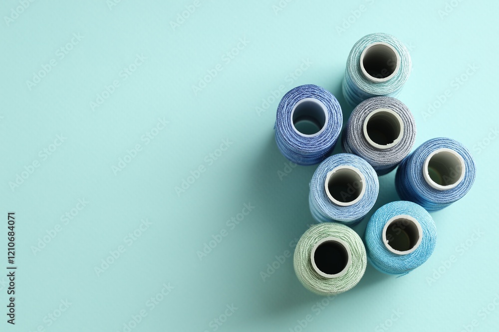 Different spools of sewing threads on light blue background, flat lay. Space for text Different spools of sewing threads on light blue background, flat lay. Space for text