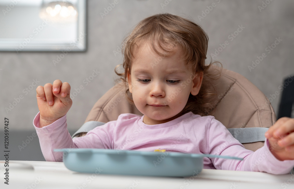 A thoughtful toddler enjoying her meal during a quiet moment at home A thoughtful toddler enjoying her meal during a quiet moment at home