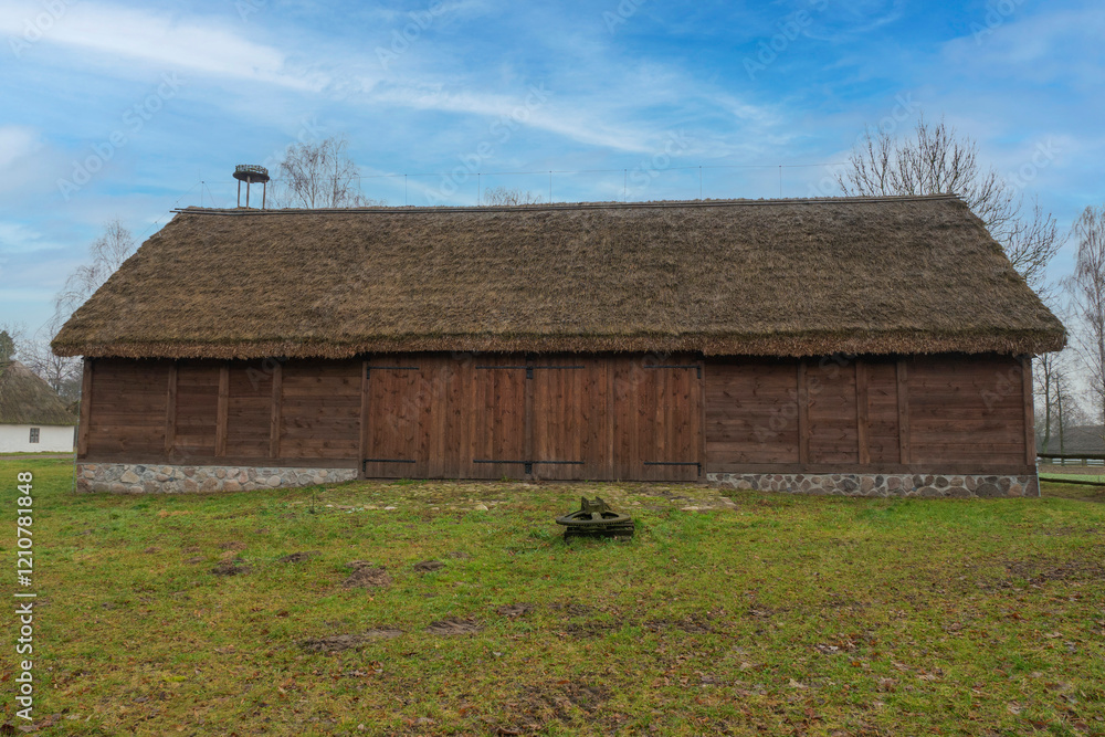 An ecological barn made of pure brown wood and a thatched roof on it, an authentic barn in a green yard amidst a blue sky, a place of strength and tranquility, a bird's nest on the roof of the barn. An ecological barn made of pure brown wood and a thatched roof on it, an authentic barn in a green yard amidst a blue sky, a place of strength and tranquility, a bird's nest on the roof of the barn.