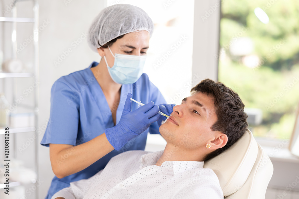 Obraz premium Young man having face mesotherapy implemented by middle-aged dermatologist in aesthetic clinic