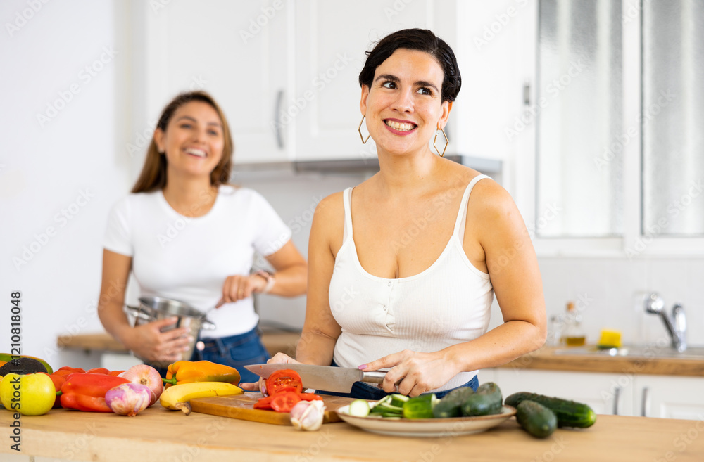 Happy cheerful female friends preparing salad and lunch together in modern kitchen
