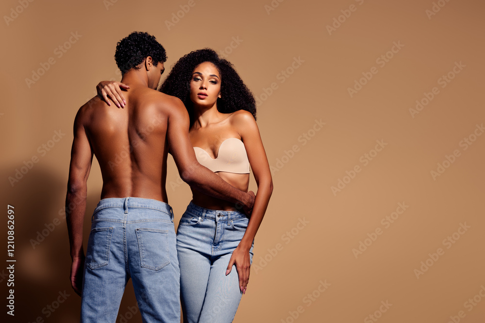Beautiful young couple embracing in studio with beige background, showcasing sensuality and modern fashion style Beautiful young couple embracing in studio with beige background, showcasing sensuality and modern fashion style