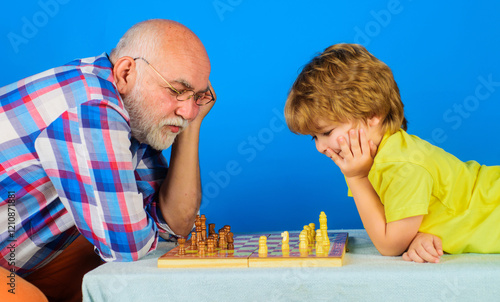 Chess competition. Grandfather and grandson playing chess. Little boy thinking about next move in game of chess. Checkmate. Childhood and logic board games. Grandpa teaching grandchild to play chess. photo