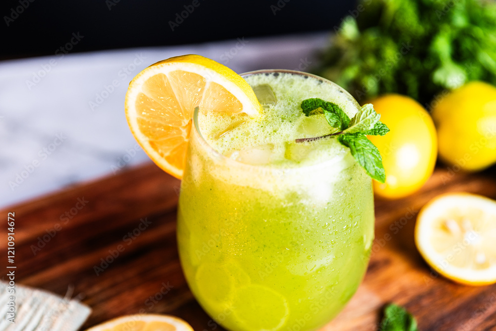 A refreshing green lemonade served in a glass with ice, garnished with mint and lemon slices, placed on a wooden board with fresh lemons and herbs in the background. A refreshing green lemonade served in a glass with ice, garnished with mint and lemon slices, placed on a wooden board with fresh lemons and herbs in the background.