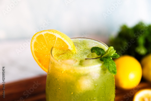 A refreshing green lemonade served in a glass with ice, garnished with mint and lemon slices, placed on a wooden board with fresh lemons and herbs in the background.