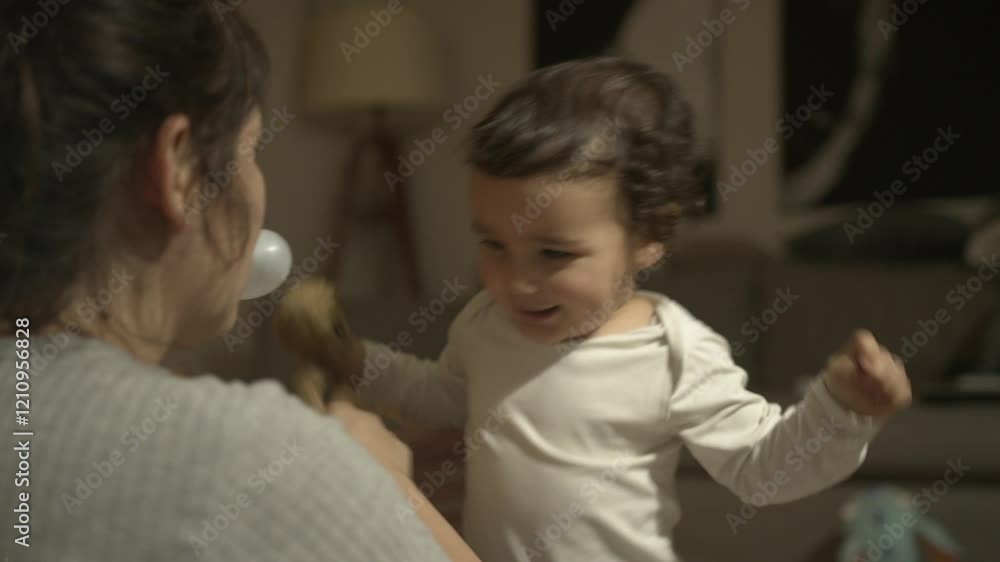 A joyful baby laughing while playing with their mother, holding a plush toy, in a warm and cozy indoor setting. A joyful baby laughing while playing with their mother, holding a plush toy, in a warm and cozy indoor setting.