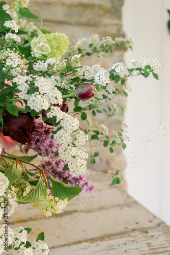 Floral arrangement in white textured compote with pink peonies, irises spirea, tulips, hydrangeas, lilacs