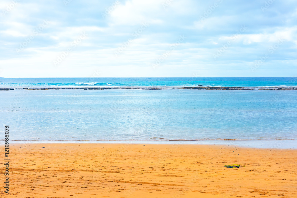 Serene beach scene with golden sand, calm turquoise waters, and gentle waves under a cloudy sky, evoking a tranquil and peaceful coastal atmosphere, perfect for relaxation and nature-themed visuals