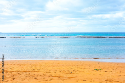 Obraz na płótnie Serene beach scene with golden sand, calm turquoise waters, and gentle waves under a cloudy sky, evoking a tranquil and peaceful coastal atmosphere, perfect for relaxation and nature-themed visuals w salonie