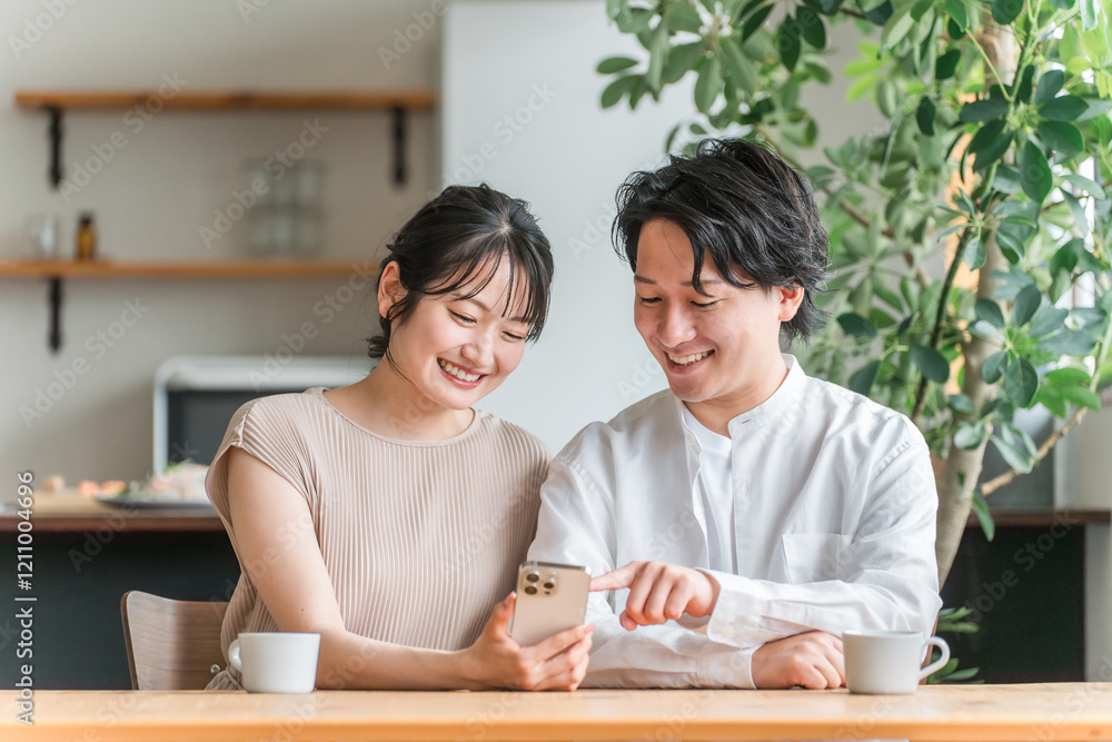 リビングダイニングでスマホを見る若いアジア人カップル
リビングダイニングでスマホを見る若いアジア人カップル