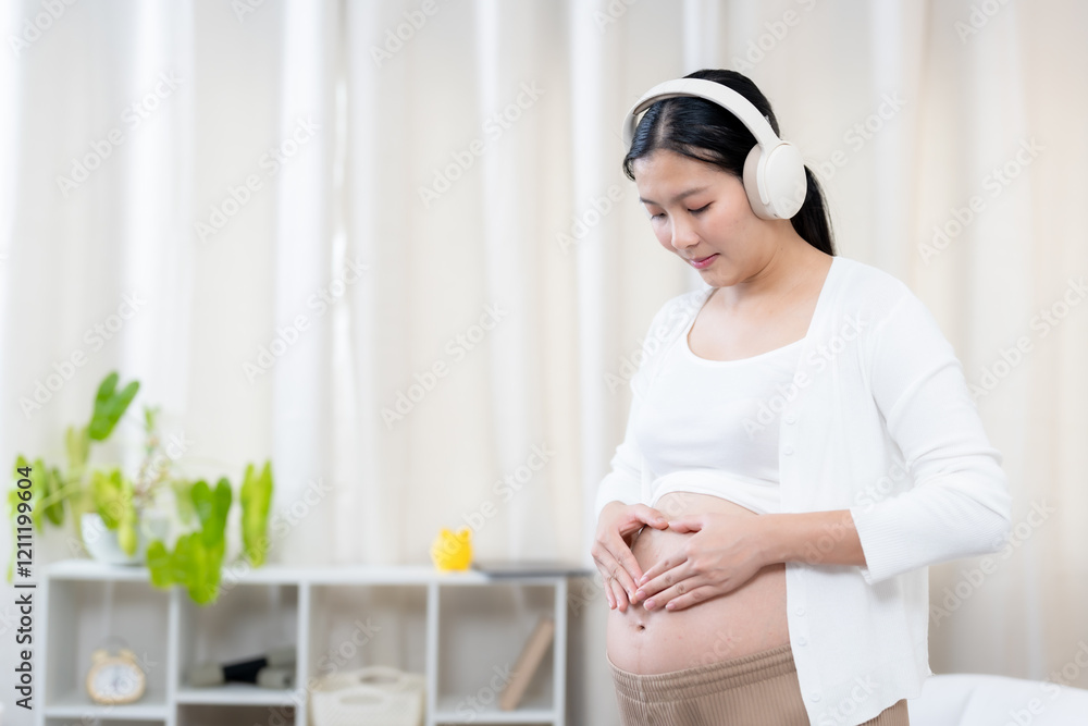 Asian pregnant woman in a serene living room setting, gently touching her belly and wearing headphones. Represents mindfulness, connection, and relaxation during motherhood journey. Asian pregnant woman in a serene living room setting, gently touching her belly and wearing headphones. Represents mindfulness, connection, and relaxation during motherhood journey.