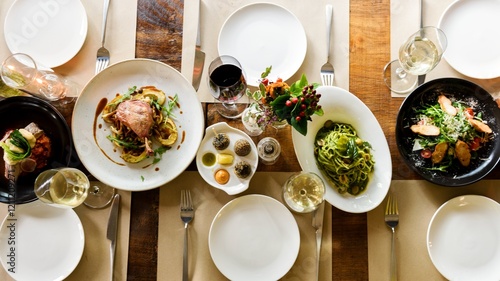 Aerial view of a dining table set with plates of pasta, salad, and meat dishes. Elegant food course with wine. The dining experience. Top view of dinning table set. Long served restaurant table