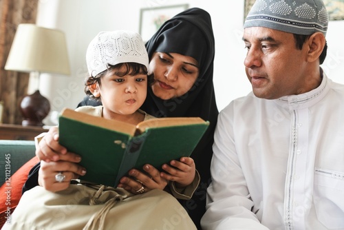 A family reading together. A child, a woman, and a man, all wearing traditional attire, focus on a book. The family shares a moment of learning and bonding. Muslim family reading the quran together. photo